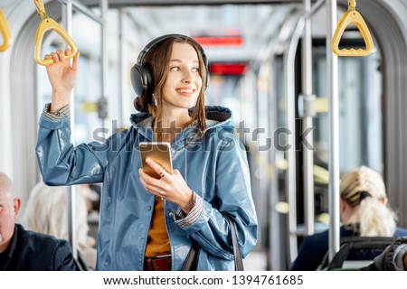 Young woman passenger standing with headphones and smartphone while moving in the modern tram, enjoying trip at the public transport Royalty-Free Stock Photo #1394761685