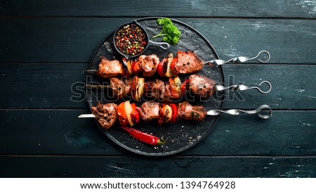 Shish kebab BBQ meat with onions and tomatoes. On a black background. Top view. Free space for your text. Rustic style. Royalty-Free Stock Photo #1394764928