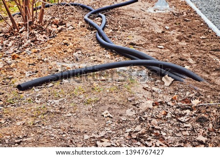 Three long black corrugated tubes lie on the ground in the park for making the connection. Royalty-Free Stock Photo #1394767427