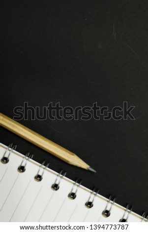 Pencil and notebook on the table, black 
 blur background.