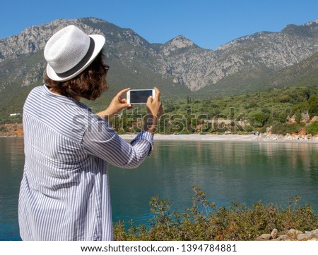 Tourist woman with white hat takes a picture of the of the Agia Kyriaki beach in the Kiparissi Lakonia village, Peloponnese, Zorakas Bay, Greece, May 2019. Daylight.