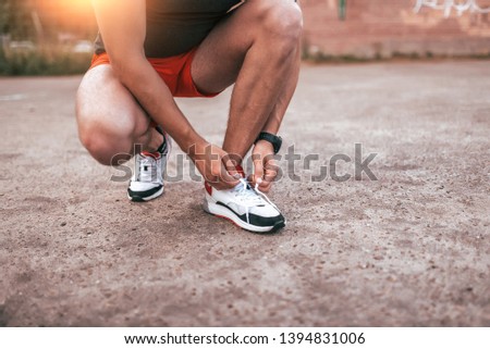 Close-up, a male athlete, tying shoelaces on sneakers. Concept of morning jogging in the city. Tanned leather, smart watch bracelet. Sportswear shorts T-shirt.