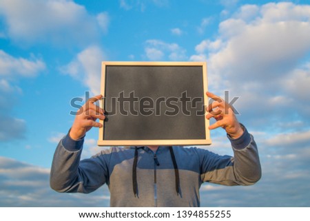 Man holding chalkboard at face level, against the sky with clouds. Copy space for your text design. billboard, chalk, advertising poster.