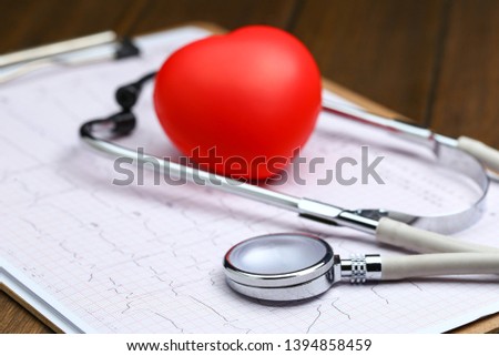 Red heart with stethoscope and electrocardiogram on wooden background