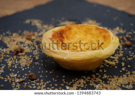 Egg tart, close up and isolated, decorated with brown sugar and pieces of chocolate cornflakes, placed on black stone plate. This photo is suitable for advertising purpose 