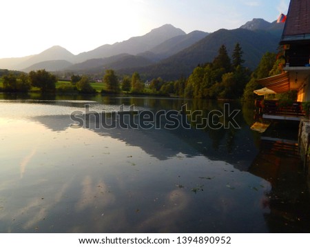                 Summer sunset view of the green Slovenian mountains from the Preddvor lake hotel's terrace, with beautiful reflection of the landscape on the water                 Royalty-Free Stock Photo #1394890952
