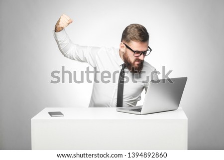 Portrait of aggressive unhappy businessman sitting in office and having bad mood are ready to punch a worker through a webcam with fist and angry face. indoor studio shot, isolated on grey background