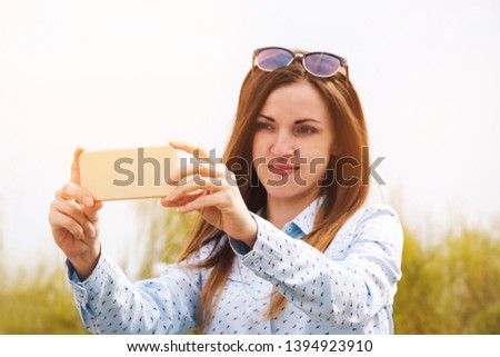 A young girl makes selfie in the park. A girl takes pictures of herself on a mobile phone in the street.