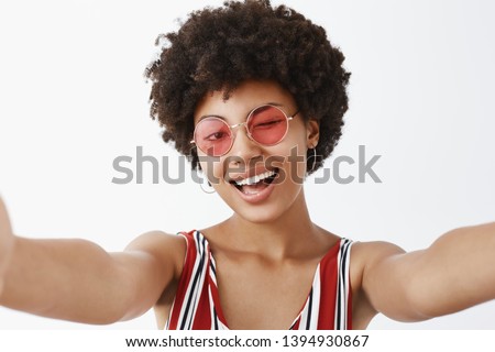 Hey, what is up. Playful hot African American with afro hairstyle, pulling hands towards camera to make selfie, winking joyfully and smiling broadly, making new profile pic for social network Royalty-Free Stock Photo #1394930867