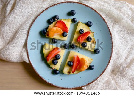 Plate with pineapple 'pizzas' - slices of pineapple with strawberries, tangerines and blueberries. Top view.