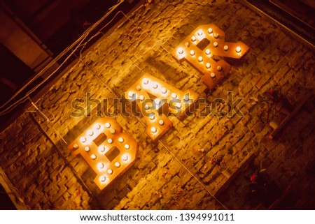 Luminous letters BAR. Volumetric letters BAR from rusty metal on a brick wall with a garland of incandescent lamps. BAR signboard. vintage photo processing.