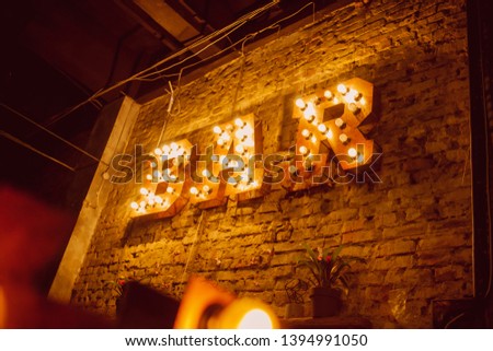 Luminous letters BAR. Volumetric letters BAR from rusty metal on a brick wall with a garland of incandescent lamps. BAR signboard. vintage photo processing.