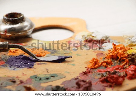 Closeup of palette with colorful paints and spatula on white surface, background or concept
