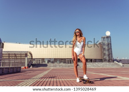 A girl in a white bathing suit body, in the summer in the city is on the street. Sunglasses skateboard longboard. Free space for text. Concept style fashion, lifestyle of young people.