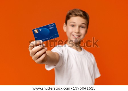 No cash money. Smiling boy showing credit card at camera, orange studio background