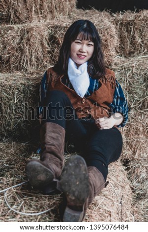Portrait of a beautiful armed Chinese female cowgirl posing on sheaves of straw