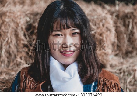 Portrait of a beautiful armed Chinese female cowgirl posing on sheaves of straw