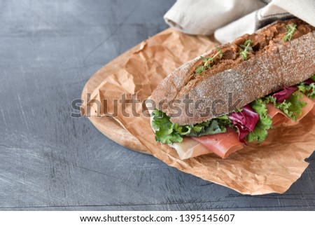 sandwich from a cereal baguette  prosciutto, lettuce, kale on a gray background. takeaway sandwich, selective focus, copy space,  takeaway lunch