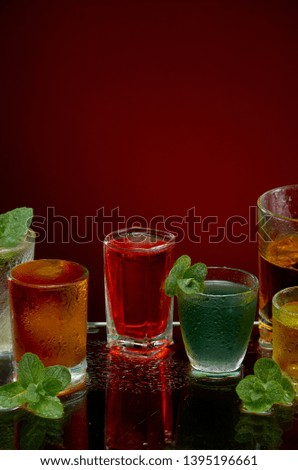 Colored alcoholic drinks with ice and mint on red background