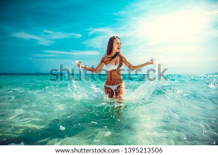 Beautiful emotional Model Girl making splash in the sea and laughing. Beautiful Woman Hot Girl enjoying the Waves of the Ocean. Tropical vacation