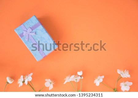 box with a gift and flowers on top of the orange background, top view