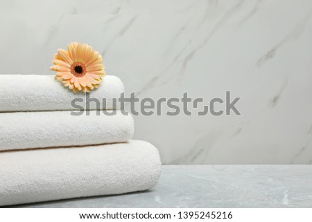 Stack of fresh towels with flower on grey table against light background. Space for text