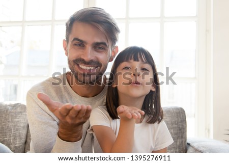 Head shot portrait of smiling father and daughter making video call together, sending blow kiss, happy dad and cute child looking at camera, saying hello or goodbye, talking at webcam at home