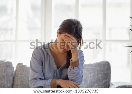 Upset young woman hiding face in hand, crying, thinking about problem, sitting alone on couch at home, girl feeling unhappy, breakup, need psychological help, offended abused, addiction trouble Royalty-Free Stock Photo #1395276935