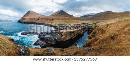 Panoramic view onto the gorge / natural harbour in Gjogv with waves hitting the cliffs and the sun in the background (Faroe Islands, Denmark, Europe)