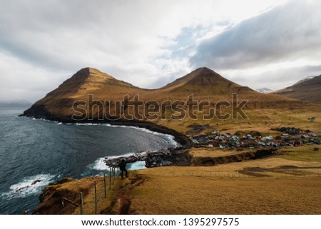 A lonely hiker on a scenic trek with spectacular views of Gjogv and its surrounding mountains and sea (Faroe Islands, Denmark, Europe)