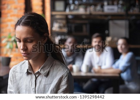 Upset mixed race woman suffering from bullying, discrimination, excluded girl having problem with bad friends, feeling offended and hurt, sitting alone in cafe, avoiding people, social outcast Royalty-Free Stock Photo #1395298442