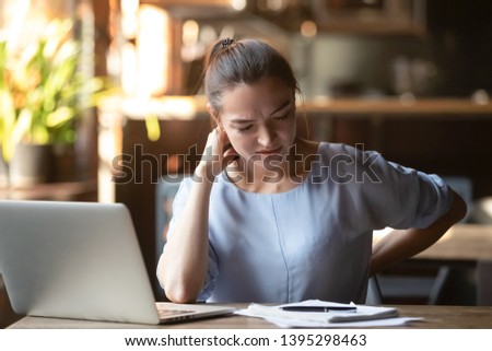 Tired woman feeling pain after sedentary computer work in uncomfortable posture or chair, exhausted female student or freelancer massaging tensed neck and back muscles, sitting in coffeehouse Royalty-Free Stock Photo #1395298463