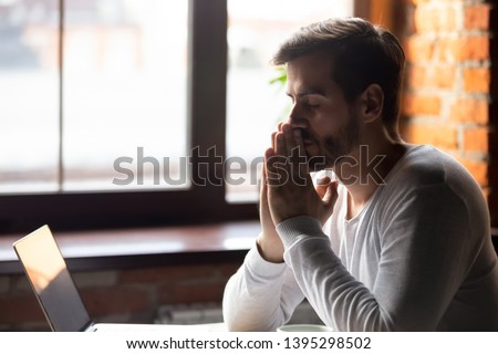 Worried man thinking about problem solution, pondering important question, puts hands together in prayer, upset sitting alone with closed eyes, frustrated about difficulties, taking break, breathing Royalty-Free Stock Photo #1395298502