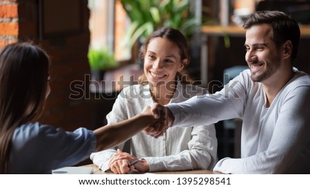 Smiling couple making successful deal, handshaking with realtor or insurance broker in cafe, family wife taking loan or mortgage, happy wife and husband at meeting with advisor or lawyer Royalty-Free Stock Photo #1395298541