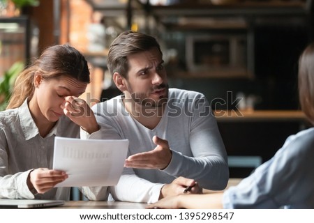 Angry young couple complaining, bad contract terms, outraged man arguing with manager or realtor, upset woman holding documents with stats, contract, dissatisfied clients demanding compensation Royalty-Free Stock Photo #1395298547