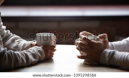 Close up woman and man sitting in cafe, holding warm cups of coffee on table, young couple spending weekend in cozy coffeehouse together, romantic date concept, visitors drinking hot beverages Royalty-Free Stock Photo #1395298586
