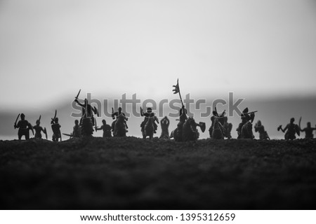 Medieval battle scene with cavalry and infantry. Silhouettes of figures as separate objects, fight between warriors on sunset foggy background. Selective focus Royalty-Free Stock Photo #1395312659