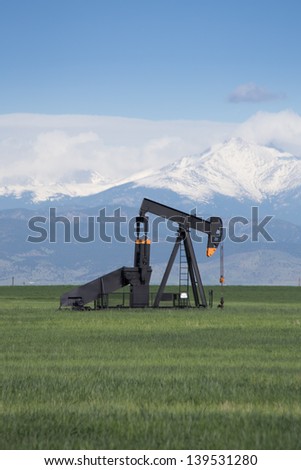 Pump Jack in Green Field With Snow Covered Rocky Mountains and Blue Sky