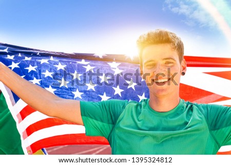 Young american man holding usa national flag outdoors - Cheerful sport fan with sun back lighting is celebrating victory  - Concept of joyful moment at competitions and events -Image