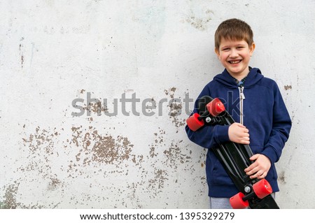 A boy in sports clothes with a skate on the background of a plastered wall.