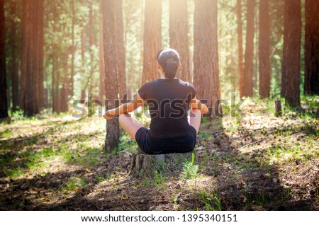 Relaxed Woman Sitting in a Comfortable, Upright Position and Practicing Meditation in the Summer Forest Among Tree Trunks. Forest Meditation Retreat for Bliss and Healing. Royalty-Free Stock Photo #1395340151