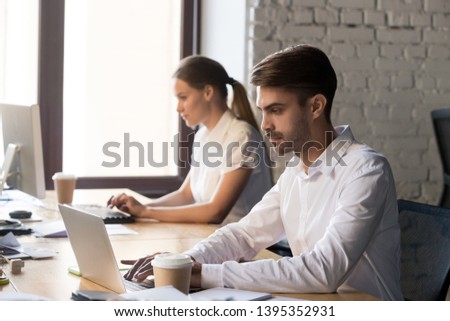 Man office worker sitting at shared desk working on computer typing business message read correspondence online communicating with corporate client solve problems checking sales statistics use program