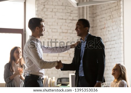 Diverse team gather at office, young boss shaking hands congratulate african employee with promotion and reward. Appreciation and gratitude, new member staff first impression, award and bonus concept Royalty-Free Stock Photo #1395353036