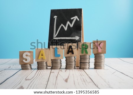 Salary increase concept. SALARY cube letter on stack of coin and chalkboard increase graph.