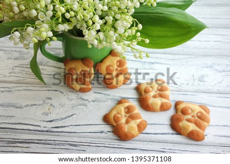 Children's shortbread cookies in the form of a panda and lily of the valley bouquet on a light wooden background.
