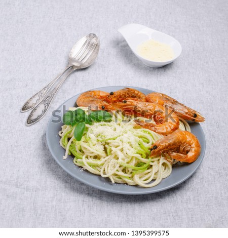 Spaghetti with zucchini and fried shrimp on textile background. Selective focus.