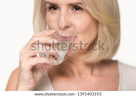 Close up studio image attractive healthy aged woman holding glass drinking enough still water, prevention dehydration in older adults, healthy habit lifestyle, helps digestion, health benefits concept