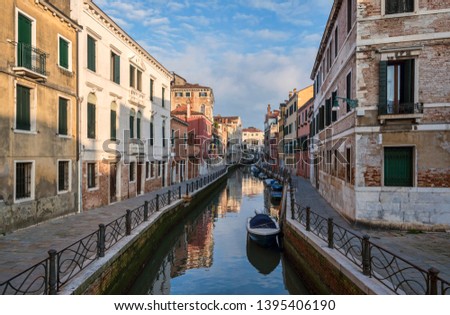 Photo of a small Venetian canal, old houses and empty sidewalks in the morning. Historic architecture of Italy. Popular travel destination in Europe