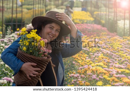 Lady wearing denim shirt holding basket with chrysanthemum flowers and one hand touching cowboy hat that she wears with background of colorful floral farm. Easy to use with copy space to use. 