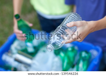 Caucasian boy and girl putting clear and green bottles and metal cans in recycling blue bin outside in yard Royalty-Free Stock Photo #139546226
